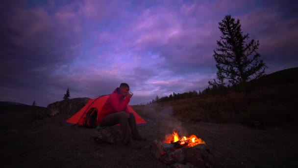 男は、キャンプの火で飲みます。旅行、夜の時間での生活 — ストック動画