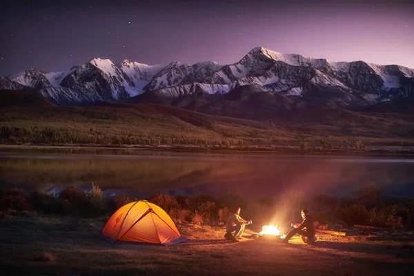 Twee mannen toeristen zitten op de verlichte tent in de buurt van kampvuur — Stockfoto