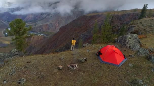 山の谷、4 k の前でテント近くに立っている男の空中映像 — ストック動画