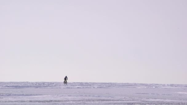 Un homme en vélo à travers un lac gelé — Video