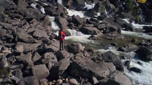 Вид з повітря на людину, що стоїть перед водоспадом з камінням, річкою — стокове відео