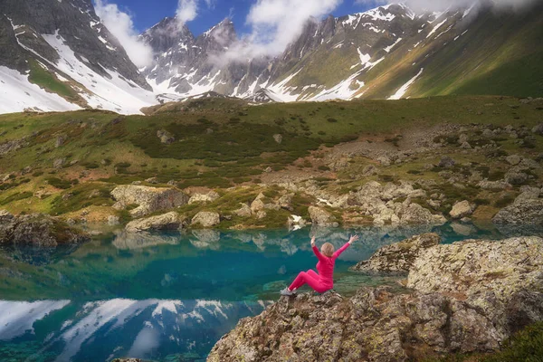 穿着红衣的远足妇女坐在高山上美丽的碧绿湖畔. 图库照片