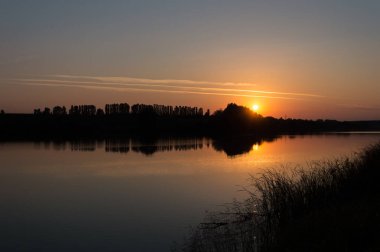 Gün batımı, siluet, ses dalgası, günbatımının sesi, ağaçların siluetinin yarattığı bir ses dalgası ve günbatımında gölün aynasındaki yansıması.