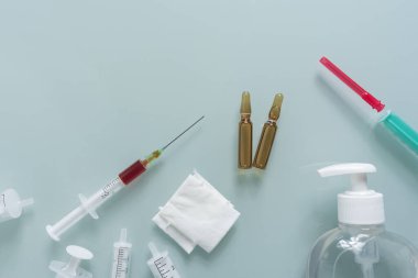 Yeşil arka planda birkaç şırınga, sargı bezi, dezenfektan ve iki ilaç kutusu var.