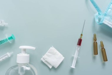 Çeşitli şırıngalar, sargı bezleri, maske, dezenfektan ve yeşil arka planda iki ilaç kutusu.