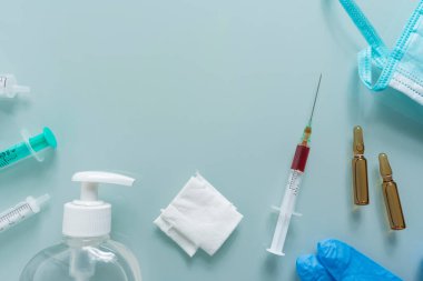 Çeşitli şırıngalar, sargı bezleri, maske, dezenfektan, eldivenler ve yeşil arka planda iki ilaç kutusu.