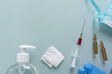 Şırınga, sargı bezi, maske, dezenfektan, eldivenler ve yeşil arka planda iki kutu ilaç.