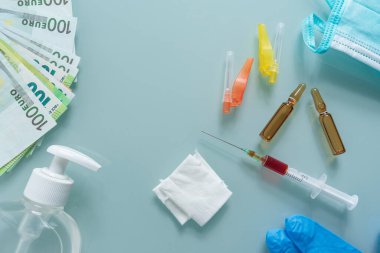 Şırınga, sargı bezi, maske, dezenfektan, eldivenler, iğneler, çok sayıda avro ve yeşil arka planda iki ilaç kutusu.