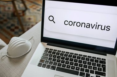 Kanepedeki dizüstü bilgisayarı kapat ve koruyucu yüz maskesi koronavirüs hakkında tarayıcı bilgilerinde arama yap. Salgın, tecrit, sahte haberler, bilgilendirme konsepti.