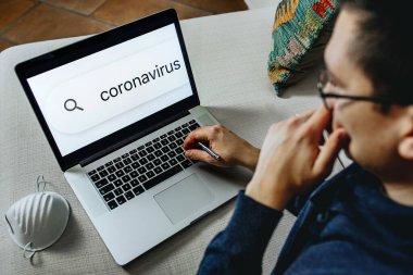 Adam evde dizüstü bilgisayar üzerinde çalışırken Coronavirus hakkında bilgi vermeye devam ediyor. Sahte haberler, internet, bilgi kavramı.