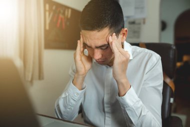 Ofiste çalışan genç bir adam baş ağrısı çekiyor. Stres ve tükenme kavramı.