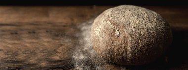 Yatay pankart çavdar ve tahıllı ekmek somunu ile ahşap masa. Soldaki metin için koyu arkaplan ve boş alan.