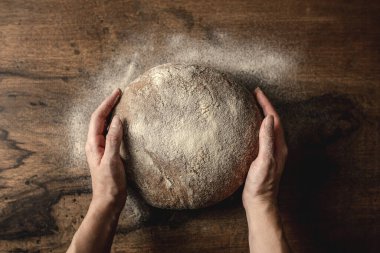 Bir somun mısır gevreğinin etrafındaki bütün ekmeği gören bir kadın. Tahta masada un var..