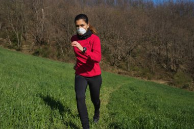 Koronavirüs salgınından dolayı yüz koruyucu maske takan genç bir kadın. Koşu, spor ve açık havada koşuyor..