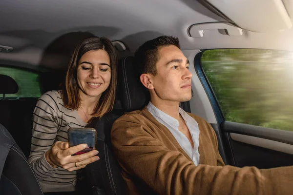 Beyaz bir çift arabanın içinde. Sürücü erkek ve elinde e-posta yazmak için akıllı telefon tutan kadın müzik veya uygulama navigasyon haritaları seçer. Hareket eden araba.