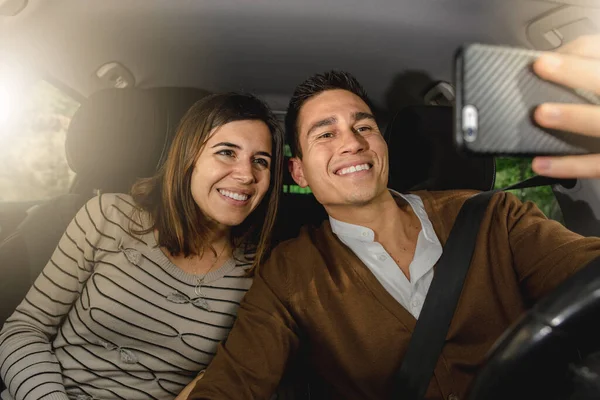 Happy caucasian couple inside car smiling while taking a selfie photo with the smartphone.