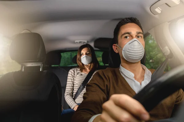 Couple inside car wearing medical protective face mask for virus protection. Social distancing and fasten seat belt. Health protection, safety and pandemic concept. Driving during coronavirus pandemic.