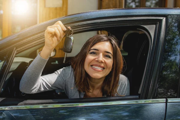 Arabadaki genç mutlu kadın pencereden bakıp gülümsüyor ve yeni arabanın anahtarını gösteriyor. Yeni ehliyet.