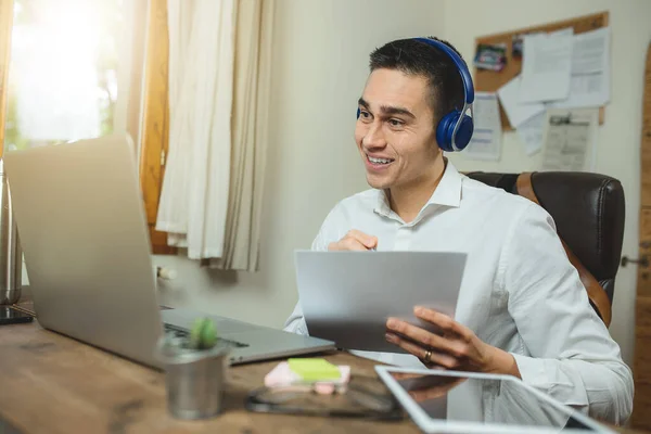 Genç iş adamının kulaklıkla iş görüşmesi var. Laptop, kağıt, gönderme, tablet ve diğer kişisel eşyaların bulunduğu çalışma yeri ahşap ofis masasında. Çağrı merkezi, işveren kavramı