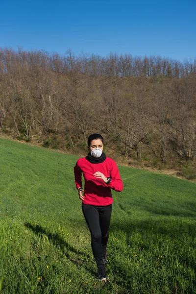 Sportive woman playing sport and running outdoor in a country-side with face protective mask for coronavirus