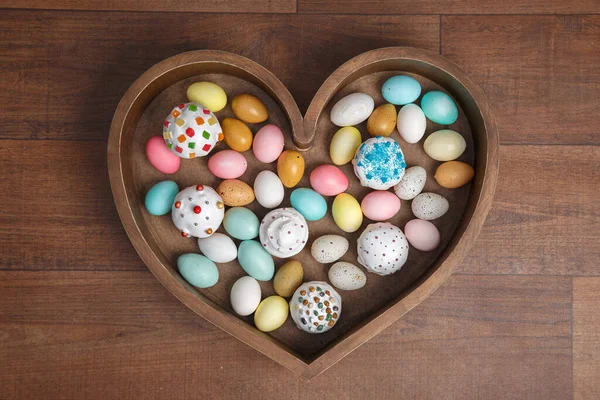 A lot of easter eggs and cake in wooden box heart form on wooden background. Spring and Easter holiday. Minimalistic design.