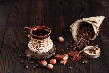 Kaliteli kil bardakta sıcak kokulu kahve ve koyu ahşap arka planda fındıklı kahve çekirdekleri.