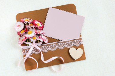 Üzerinde yabani pembe çiçekler olan bir zarf ve arka planda beyaz bir kart, Anneler Günü.