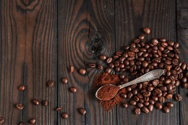 Çuval bezinde kavrulmuş aromatik kahve çekirdekleri, koyu ahşap arka planda, kaşıkta öğütülmüş kahve.