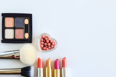 Dekoratif kozmetik ürünleri, ruj, allık ve makyaj fırçaları beyaz bir yüzeyde uzanır.