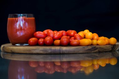 Gerçek bir İtalyan pizzası hazırlamak için siyah arka planı ve aynalı yüzeyi olan ahşap kesme tahtasının üzerinde kırmızı ve sarı bir grup vişneli domates.