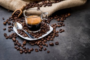 Siyah bir zeminde, kahve çekirdekleri ışık kesen cam bir fincanda İtalyan espresso kahvesi