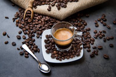 Siyah bir zeminde, kahve çekirdekleri ışık kesen cam bir fincanda İtalyan espresso kahvesi