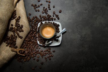 Siyah bir zeminde, üzerinde kahve çekirdekleri olan camdan bir fincanda İtalyan espresso kahvesi.