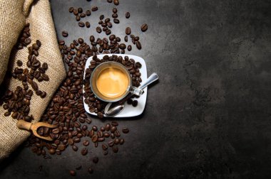 Siyah bir zeminde, üzerinde kahve çekirdekleri olan camdan bir fincanda İtalyan espresso kahvesi.