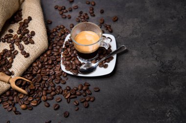 Siyah bir zeminde, üzerinde kahve çekirdekleri olan camdan bir fincanda İtalyan espresso kahvesi.