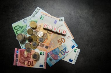 Koyu bir yüzey ve COVID üzerinde euro banknotları ve madeni paralar