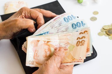 Eski el, Türk Kağıt Parası 'nı cüzdanda, beyaz arka planda madeni para ve şekerlerle tutuyor.