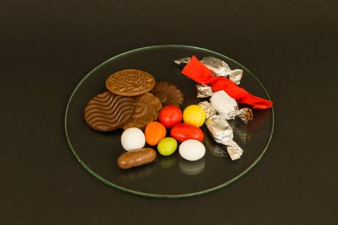 Lezzetli çikolata ve renkli şekerler, siyah yüzeyde cam tepside..