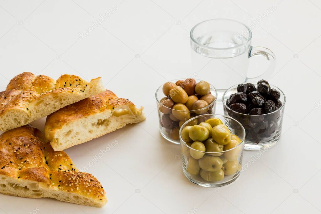 Fresh Ramadan breads sliced on white background with olive varieties and a glass of water.