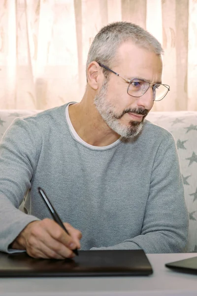 Dijitalleştirici tabletli gözlüklü adam oturma odasındaki fotoğrafları tab ediyor.