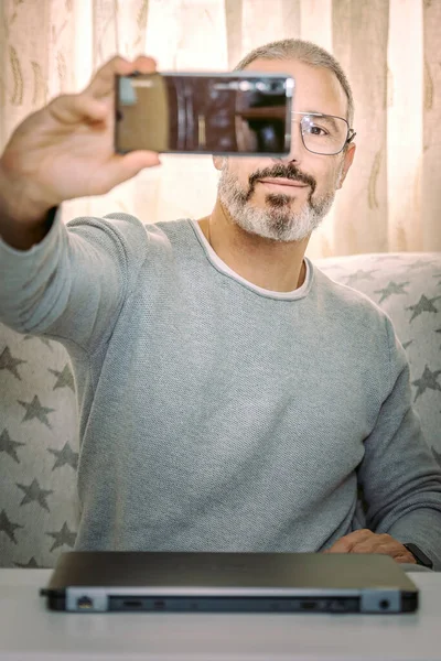 Oturma odasında selfie çeken gözlüklü bir adam sosyal ağlarına göndermek için.