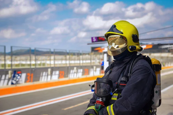 Sarı başlıklı ve yansıtıcı bakışlı itfaiyeci güpegündüz yarış pistini izliyor.
