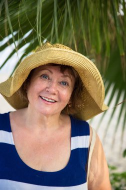 Gülümseyen kıdemli womanwearing şapka palmiye ağaçları altında