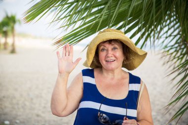 Gülümseyen kıdemli womanwearing şapka palmiye ağaçları altında