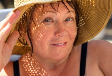 Gülümseyen kıdemli kadın kumsalda şapka