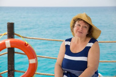 Gülümseyen kıdemli kadın iskelede lifebuoy ile plajda şapka
