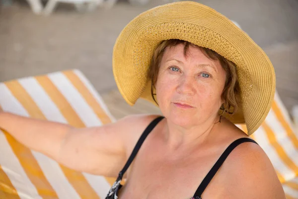 Gülümseyen kıdemli kadın plajda şezlong üzerinde şapka