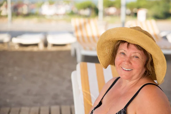 Smiling Senior woman wearing hat at beach on sunbed — Stock Photo, Image