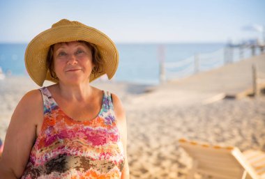 Gülümseyen kıdemli kadın plajda şezlong üzerinde şapka