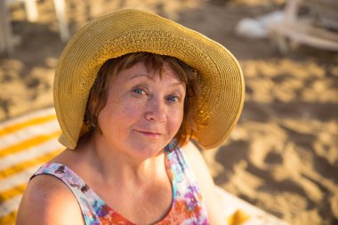 Gülümseyen kıdemli kadın plajda şezlong üzerinde şapka